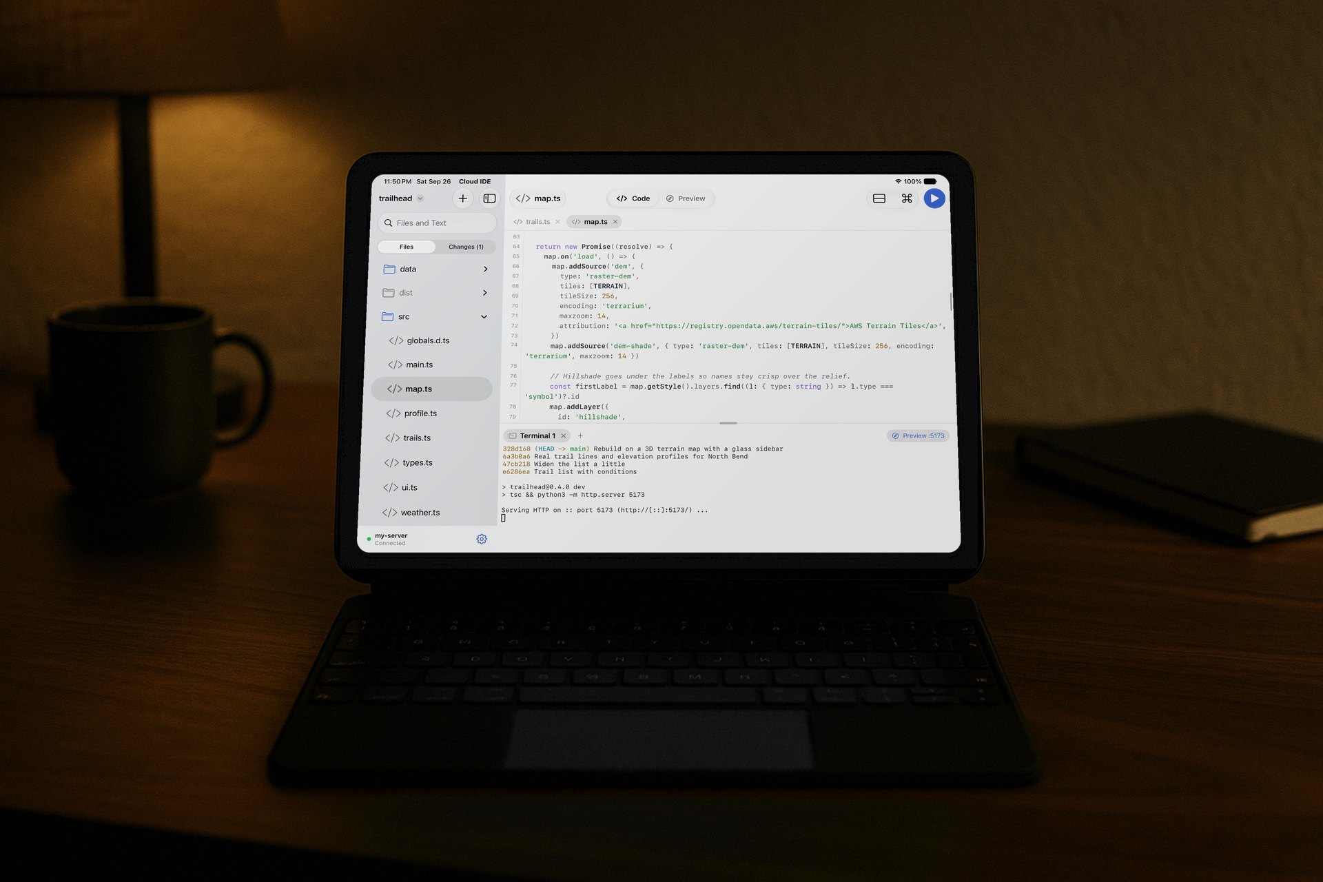 An iPad with a keyboard on a desk at night, with map.ts from the Trailhead project open in the Serin Cloud IDE editor and its dev server running in the terminal.